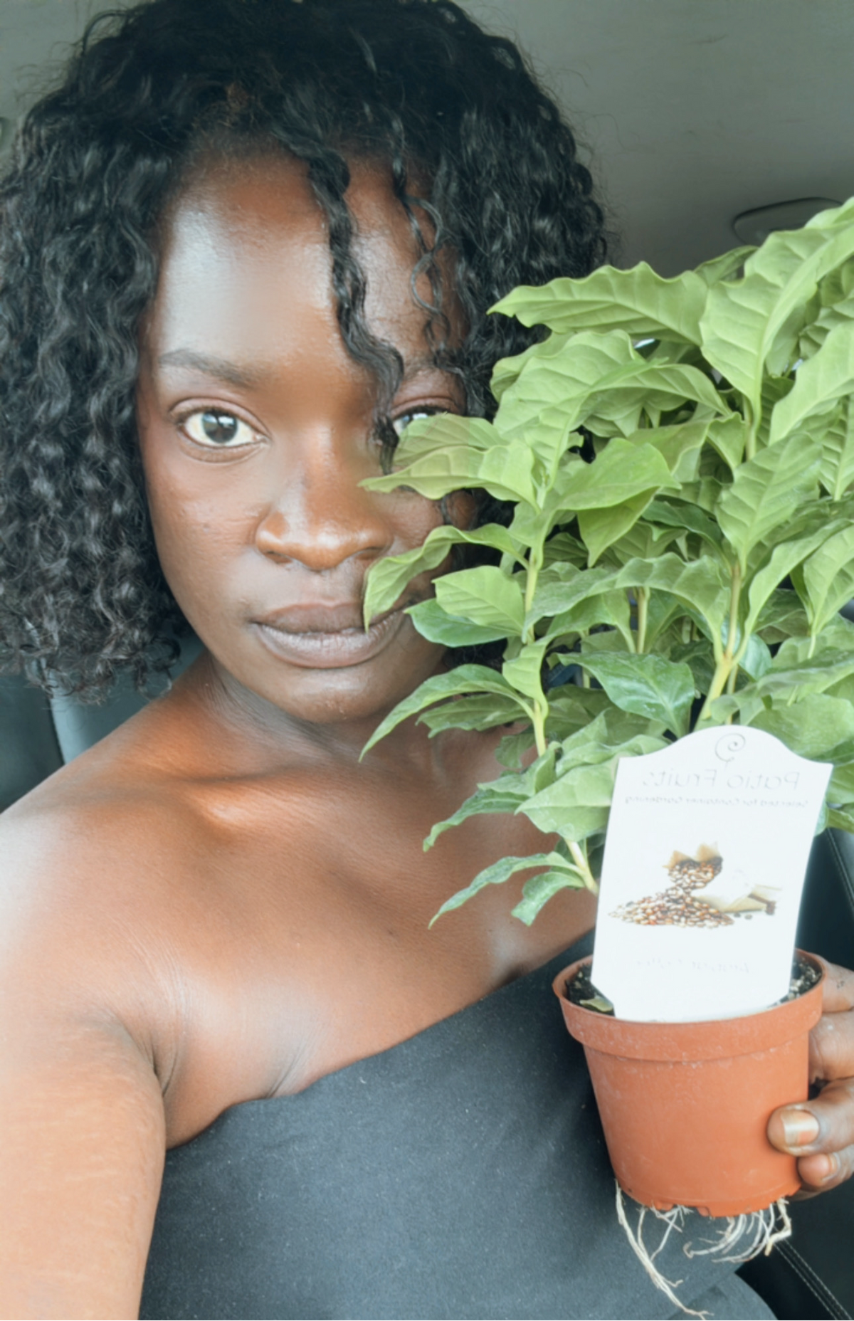 A woman holding a small potted coffee plant beside her face.