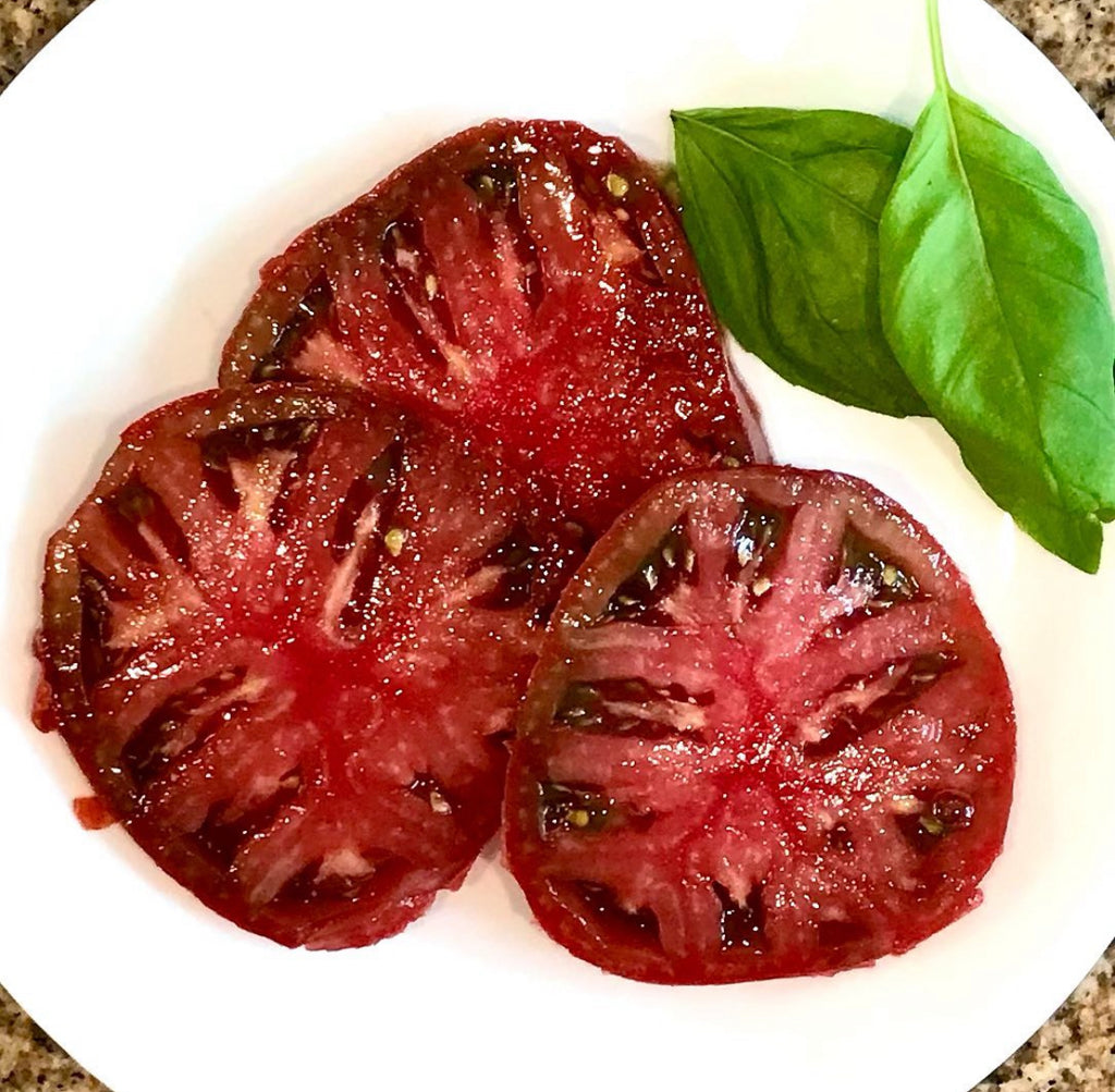 Thick slices of dark red tomato on a white plate with a basil leaf.