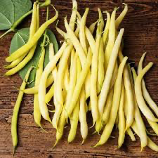 Pale yellow wax beans scattered on wood beside green leaves.