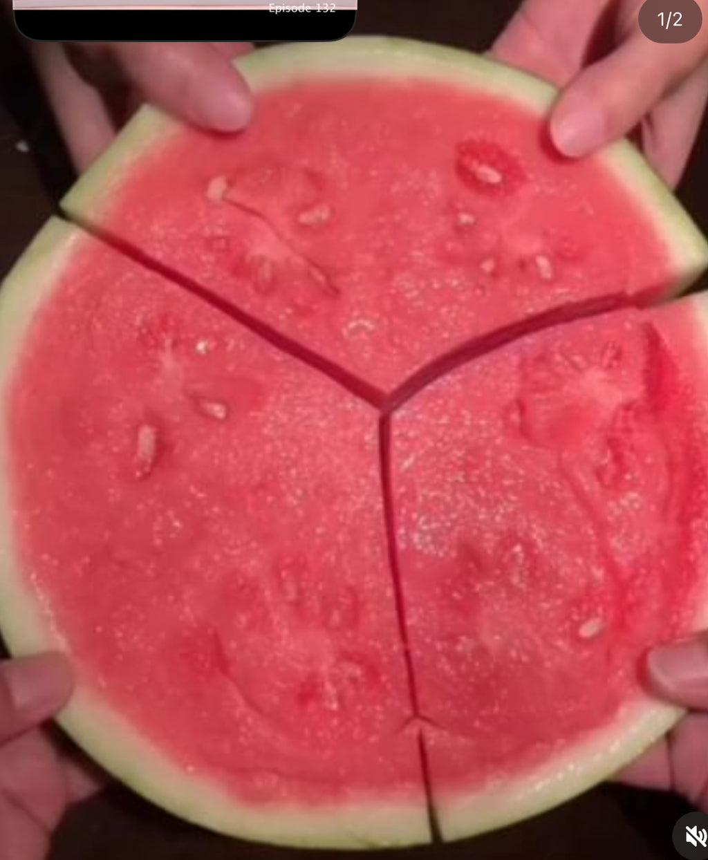 Hands holding a round slice of watermelon cut into three red-fleshed sections.