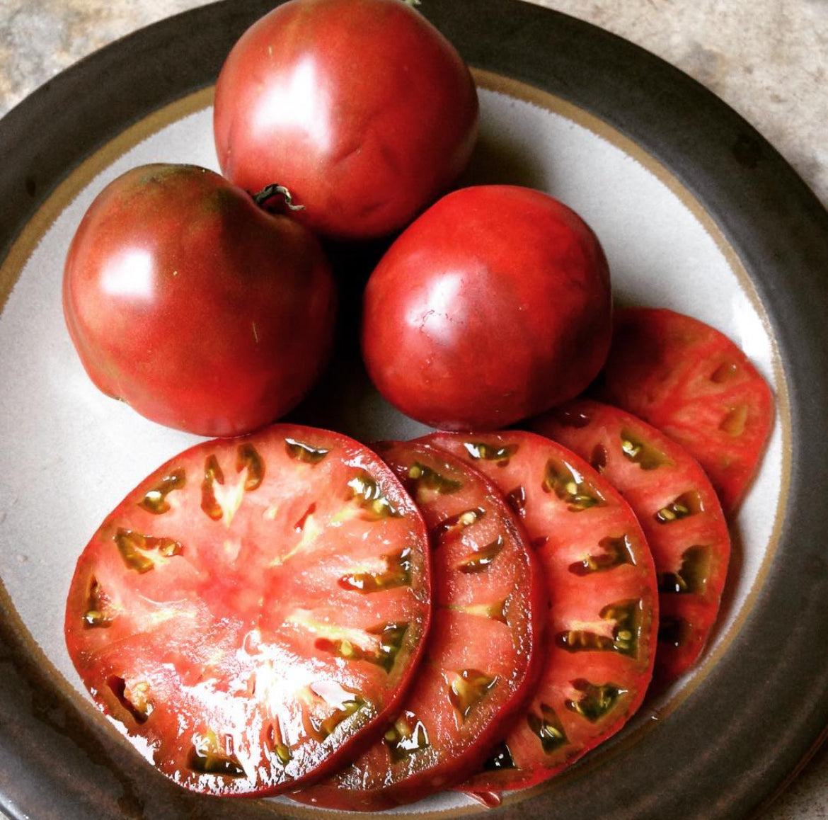 Whole tomatoes and overlapping tomato slices on a plate.