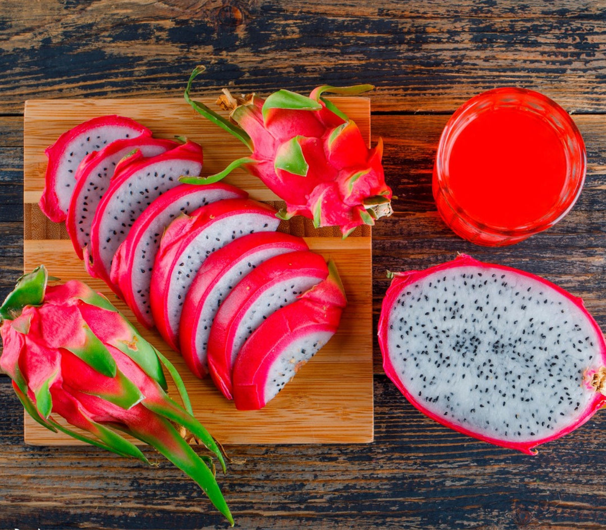 Pink dragon fruit, white-fleshed slices, and a glass of red liquid on a wooden surface.