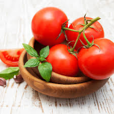 A wooden bowl of red tomatoes with green leaves and a cut wedge.