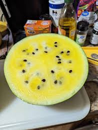 A yellow-fleshed watermelon half resting on a kitchen cutting board.