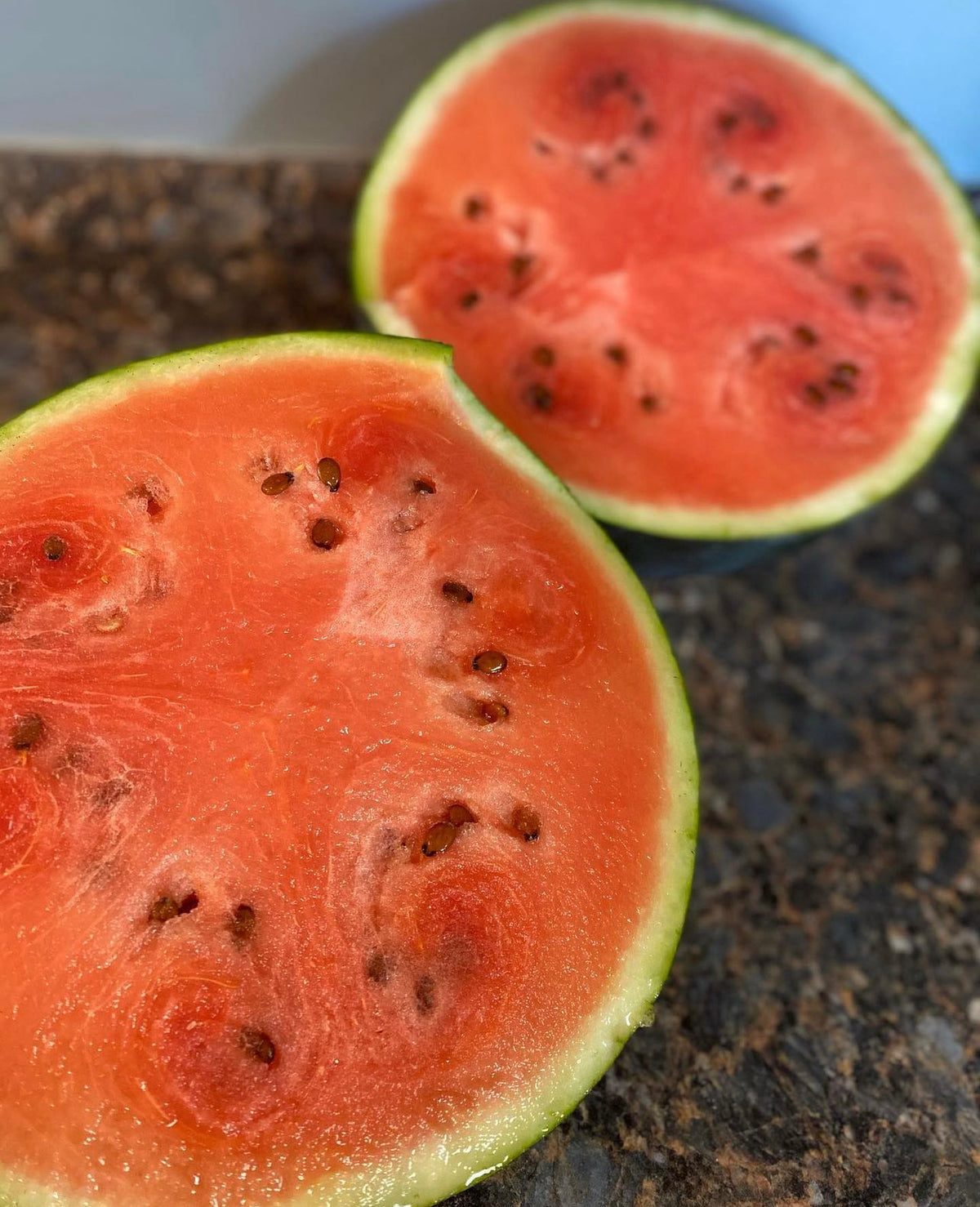 Two red-fleshed watermelon halves resting on a kitchen counter.