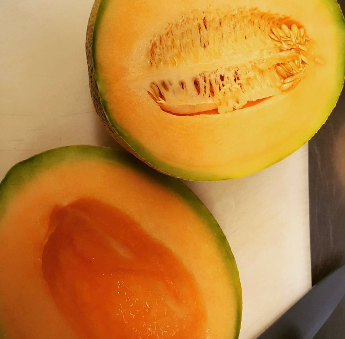 Two melon halves on a cutting board, one with its seeds removed.