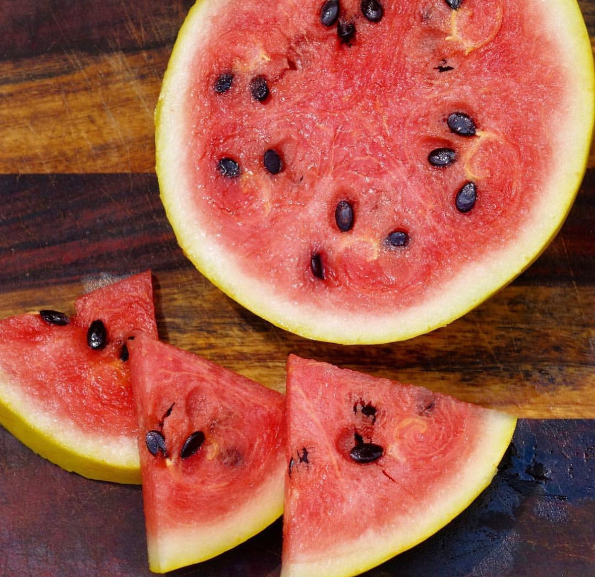 A red-fleshed watermelon half and wedges arranged on a wooden board.