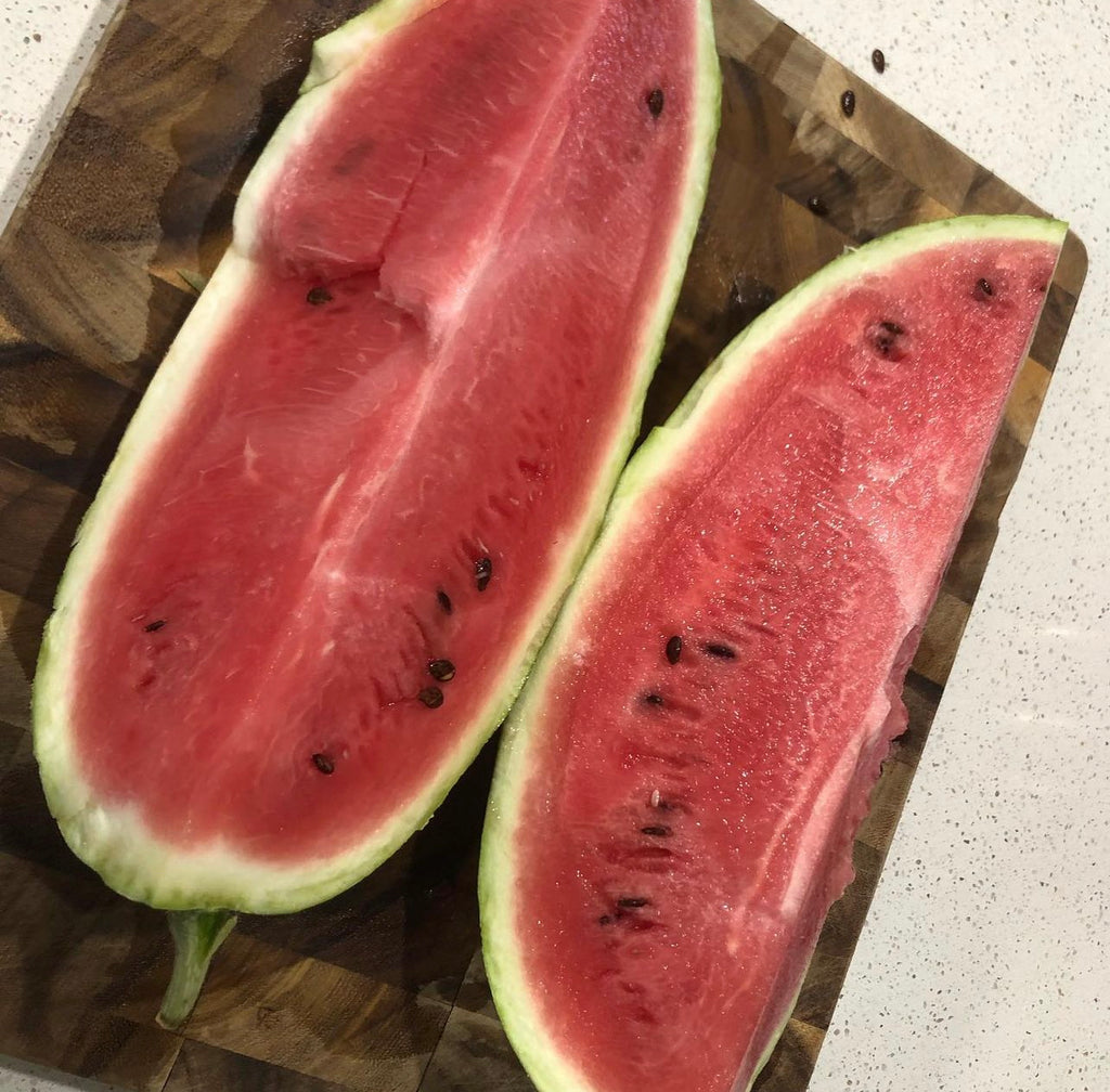 An elongated All Sweet watermelon cut lengthwise into red-fleshed halves — from BlackOwnedSeeds.com.