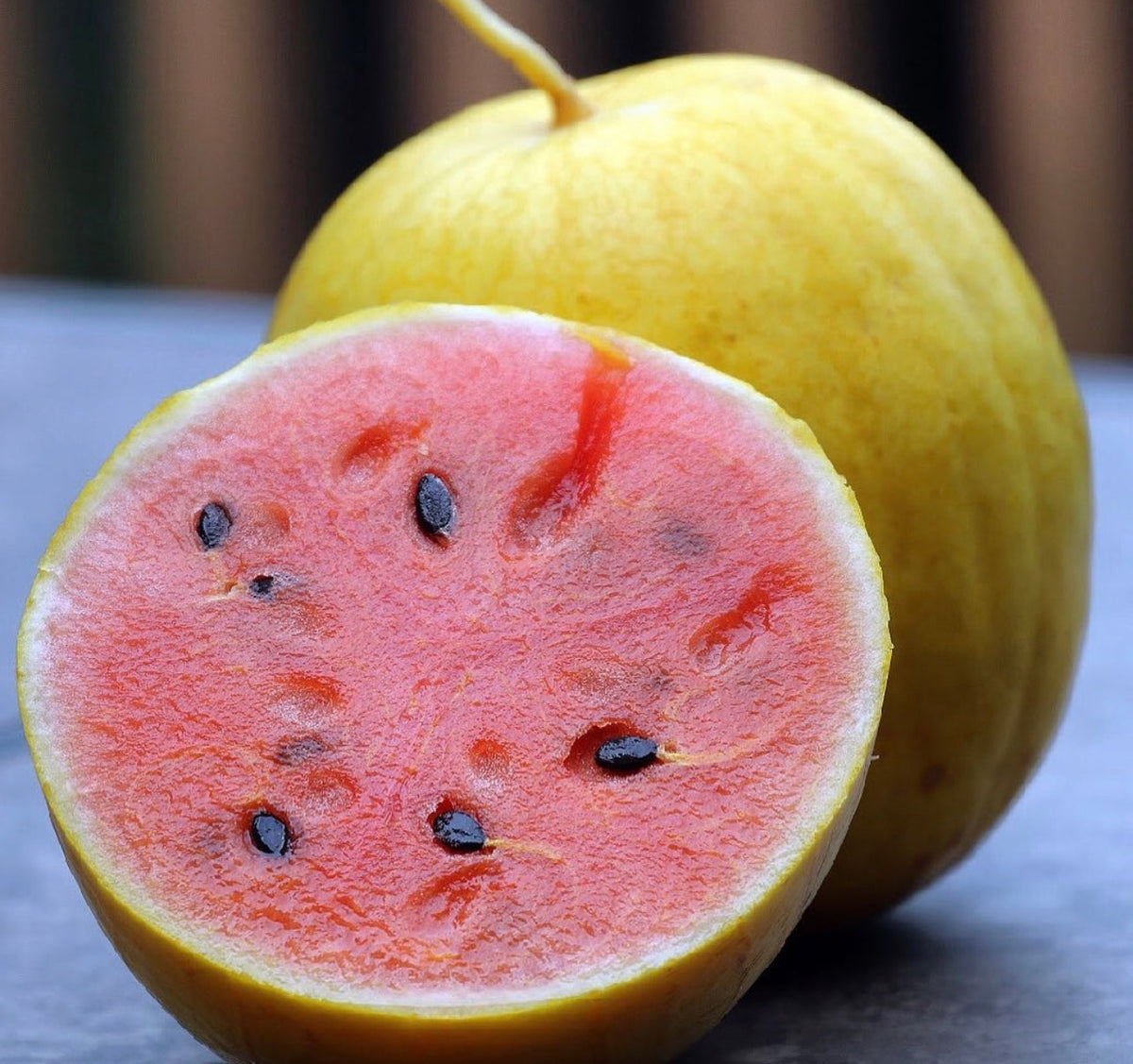 A whole yellow-rind watermelon beside a cut half showing pink-red flesh.