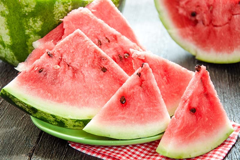 Early Crimson Treat watermelon cut into red wedges on a picnic table — from BlackOwnedSeeds.com.