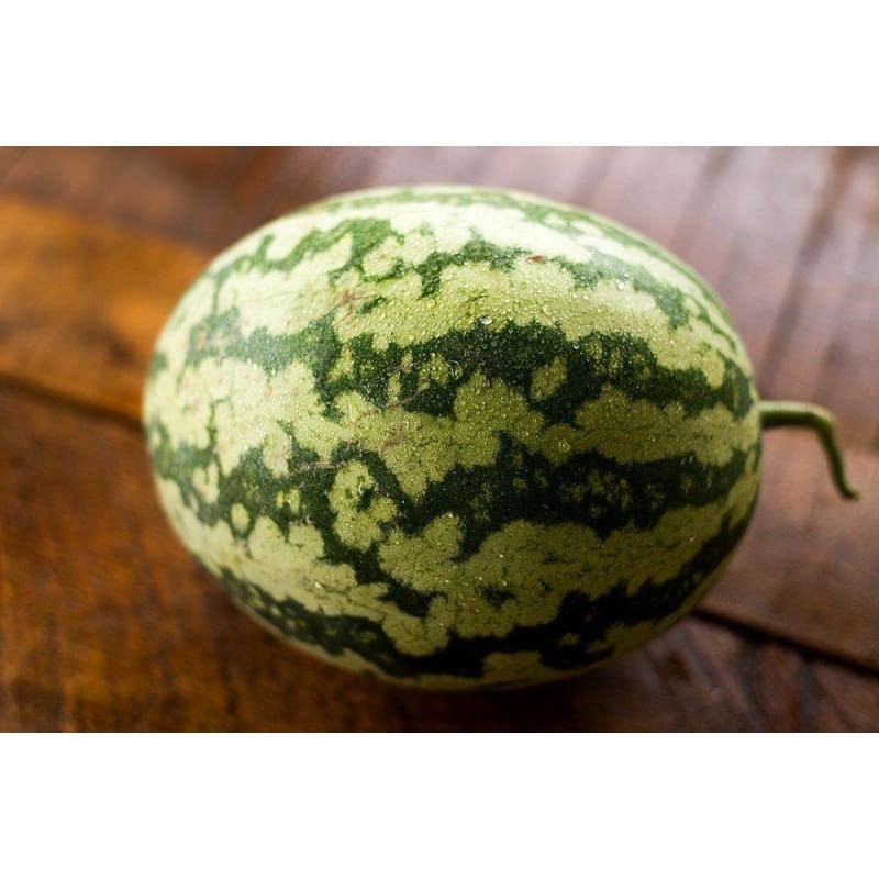 A green-striped watermelon resting on a wooden surface.