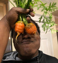 A person holding two round orange Parisienne carrots over their eyes — from BlackOwnedSeeds.com.
