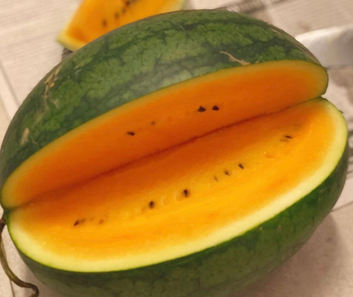 An orange-fleshed watermelon cut open to show its dark seeds.